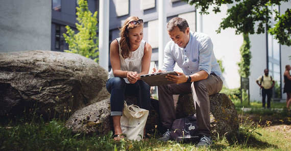 Masterstudium für das Lehramt in beruflichen Fächern der Sekundarstufe II möglich. Zwei Studierende sitzen auf dem Campus und schauen auf ein Tablet.