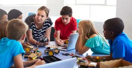 Eine Gruppe von jungen Schüller*innen umringt eine Lehrperson, die ihnen etwas erklärt.