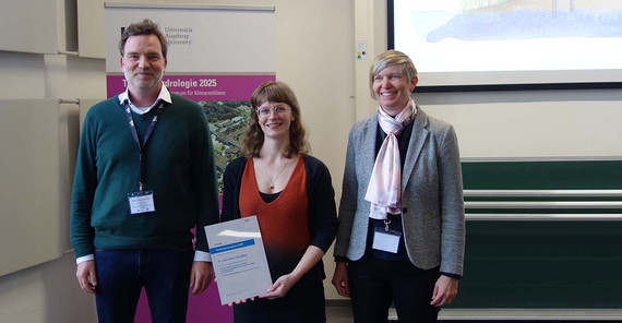 Foto von drei Personen, die bei einer Preisverleihung zusammenstehen