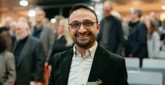 Ein Mann steht mit Blumenstrauß und Auszeichnung in einem Hörsaal