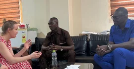 Zwei Männer und eine Frau sitzen auf Sofas und sprechen miteinander.