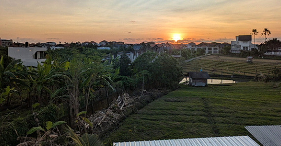 Sonnenuntergang auf Bali von einer erhöhten Position aus fotografiert. Eine Szene mit Palmen und Häusern.