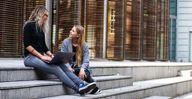 Zwei junge Frauen sitzen auf einer Treppe und unterhalten sich.