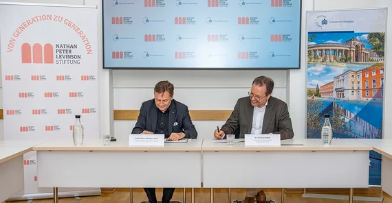 Zwei Männer sitzen an einem Tisch und unterschreiben etwas.