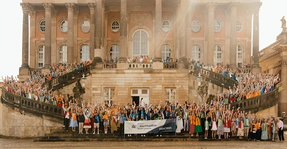 Gruppenbild hunderter Absolventinnen und Absolventen auf der Freitreppe der Communs am Neuen Palais in malerischem Licht.