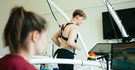 Pietro Delli Guanti auf dem Laufband Eine junge Frau schaut auf einen Bildschirm. Hinter ihr läuft ein junger Mann auf einem Laufband. Er ist verkabelt und mit einem Seil gesichert.