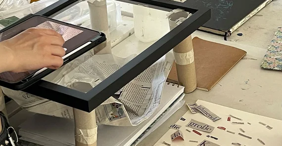Blick auf die Arbeitsfläche einer studierenden Person: Digitale Kunst entseht aus Zeitungsartikeln.