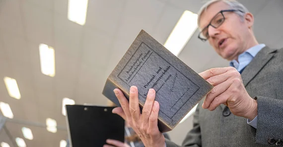 Ralf Müller hält das Personalverzeichnis der Pädagogischen Hochschule aus dem Studienjahr 1949/50 in den Händen.