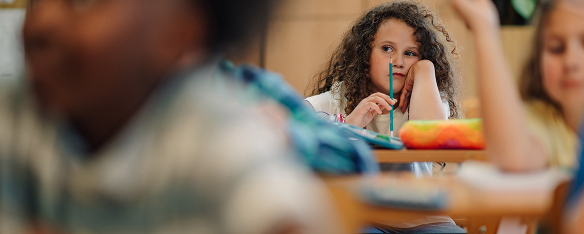 Kind sitzt in einem Klassenraum hinter anderen Kindern - 