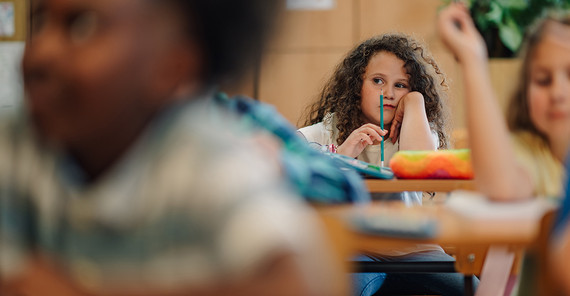 Kind sitzt in einem Klassenraum hinter anderen Kindern