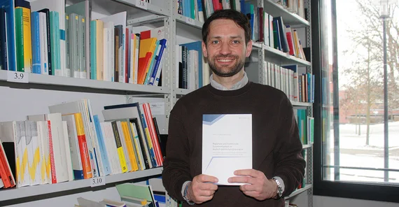 Dr. Peter Ulrich mit seinem Buch vor einer Bücherwand stehend.