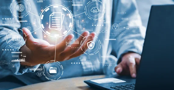 Eine Hand mit visualisierten Daten vor einem Laptop