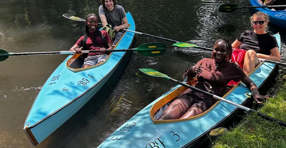 Zwei Kanus im Wasser. Darin sitzen Personen und lachen.