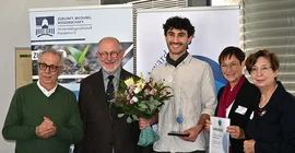 Fünf Personen stehen nebeneinander. Der Preisträger Rohan Sawahn steht in der Mitte und hält einen Blumenstrauß.