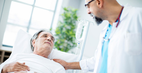 Behandelnder Arzt steht am Krankbett seines Patienten.