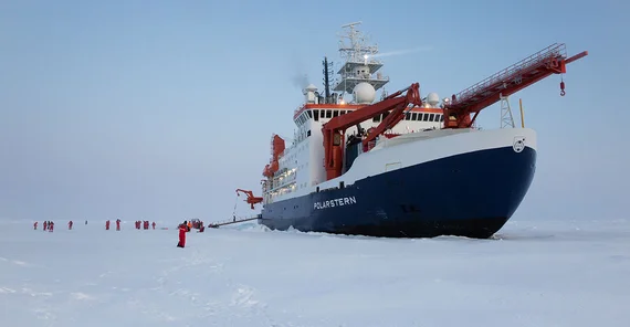Das Forschungsschiff "Polarstern" im ewigen Eis. Neben ihr klein erscheinend arbeiten Expdeditionsteilnehmende.