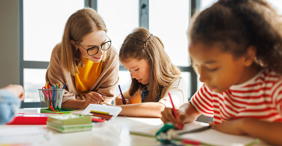 Eine Lehrerin hilft einer Schülerin, daneben sitzt eine zweite Schülerin