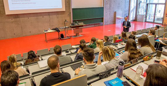 Blick in einen Hörsaal von hinten über die Köpfe der Studierenden auf den vortragenden Wissenschaftler