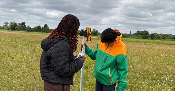 Zwei Personen bei Vermessungen im Feld.