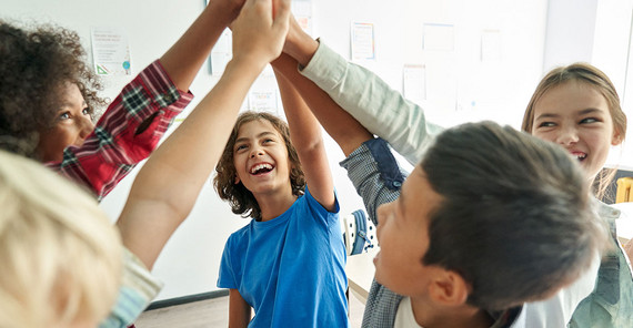 Der Wert von Mehrsprachigkeit sollte noch stärker bewusst gemacht und genutzt werden. Kinder stehen in einem Kreis zusammen und strecken ihre Hände nach oben.
