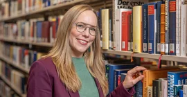 Frau steht an einem Bücherregal