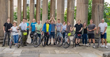 Eine große Gruppe von Menschen posiert breit aufgestellt, teils mit Fahrrädern, für ein Gruppenfoto.
