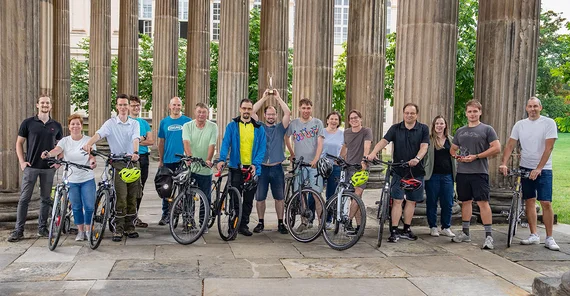 Eine große Gruppe von Menschen posiert breit aufgestellt, teils mit Fahrrädern, für ein Gruppenfoto.
