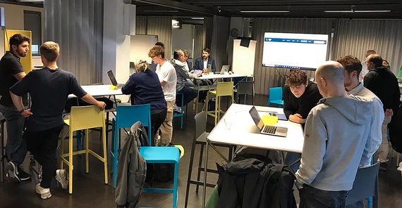 Menschen stehen an Tischen in einem Raum und reden miteinander