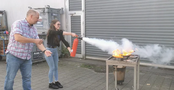 Brandschutzübung im Rahmen der Erstunterweisung in Arbeits- und Umweltschutz. Eine Person löscht unter Anleitung des Leiters des Sicherheitswesens der UP einen kontrollierten Brand in einem Topf mit einem Feuerlöscher.