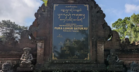 Tafel mit traditioneller Schrift am Pura-Luhur-Batukau-Tempel. Der Hintergrund der Tafel ist schwarz glänzend, die Schrift goldfarben.
