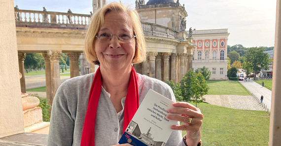 Foto einer Frau an einem Fenster mit einem Buch in der Hand