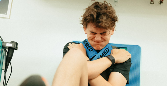 Flynt Schuring gibt alles auf der Beinpresse Ein junger Mann mit dunklen Haaren sitzt mit vor der Brust gekreuzten Armen auf einem Sitz. Er drückt mit einem Bein ein Gewicht weg, wobei er die Backen aufbläst und die Augen zukneift.