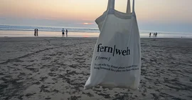 Strand in Seminyak im Hintergrund. In den Vordergrund wird ein Jutebeutel mit dem Aufdruck "fernweh" gehalten.