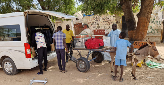 Im Dienste der Forschung: Ein Esel transportiert die technische Ausrüstung. Fünf Personen stehen vor einem weißen Transporter und verladen technische Ausrüstung auf einen Esel der einen Wagen zieht.
