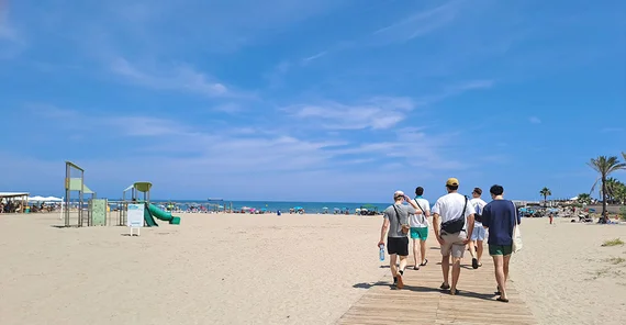 Strandszene in Weitwinkelaufnahme: Studierende, die von der Kamera weg gen Meer laufen.
