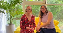 Zwei Frauen sitzen auf einer Fensterbank und schauen in die Kamera