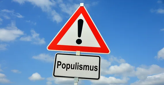 Dreieckiges Warnschild mit Ausrufezeichen, darunter Hinweisschild mit dem Begriff "Populismus". Beide vor blauem Himmel mit Wolken.