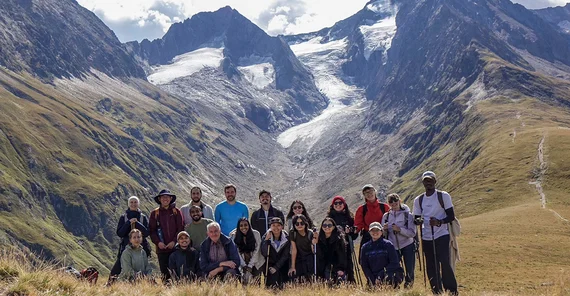 Eine Gruppe von Menschen posiert vor hohen Bergen im Hintergrund für ein Gruppenfoto