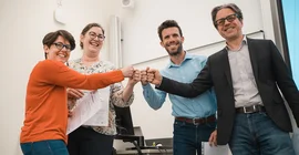 Vier Menschen stehen im Kreis und strecken ihre Fäuste in die Mitte