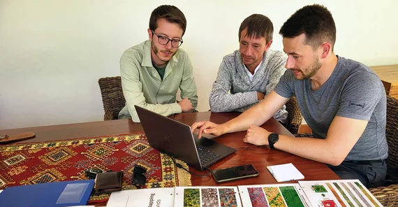 Drei Männer sitzen an einem Tisch und schauen in einen Laptop