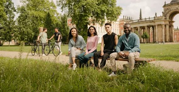 Vier junge Menschen sitzen auf einer Bank auf dem Uni-Campus Am Neuen Palais