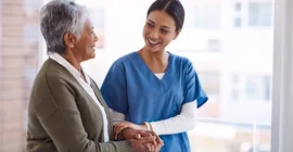 Eine Pflegerin stützt eine ältere Frau.