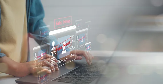 Laptop mit einer Hand, die ihn bedient, darüber der Schriftzug Fake News