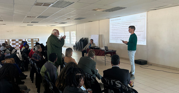 Rund 20 Menschen sitzen in einem Raum, einer steht vorn, sie diskutieren miteinander