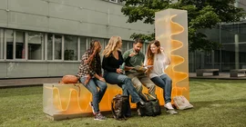 vier junge Menschen sitzen auf einer Bank im Innenhof eines Hauses