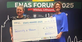 Zwei Personen halten einen übergroßen Check zusammen vor sich. Beide lachen in die Kamera.