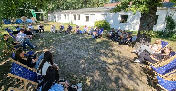 Lunch im Grünen mit Unterstützung der BARMER. Ein Stuhlkreis aus Liegestühlen im Freien. Menschen sitzen in den Stühlen und unterhalten sich.