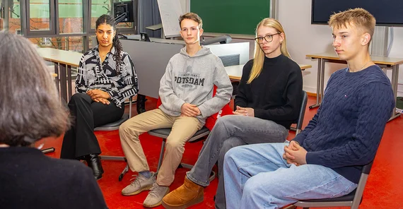 Four students are sitting on chairs listening to a lecture.