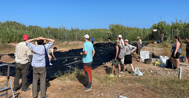 Eine Gruppe Menschen beim Abdecken des Grabungsareals.