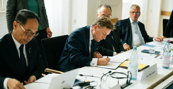 mehrere Männer, die an einem Tisch etwas unterschreiben